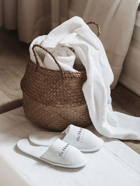 Woven laundry basket with fresh white towels and branded slippers in a minimal guest bedroom at House 33 Sapanca.