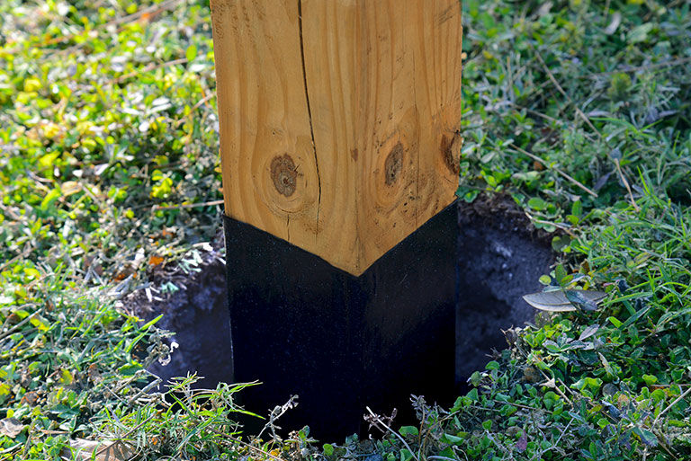 Close-up of pressure-treated fence post protected with waterproof barrier at ground contact area.