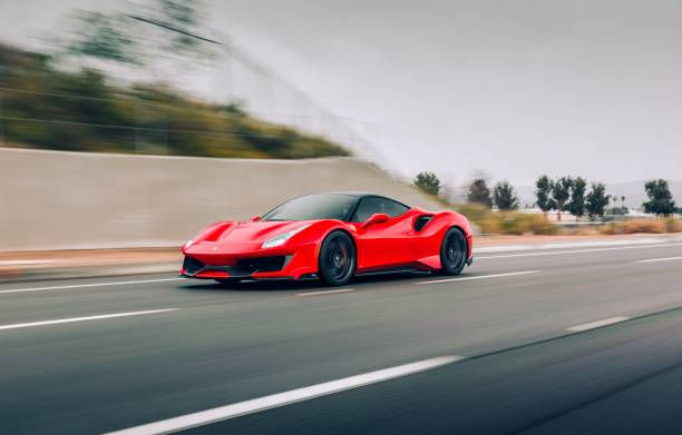 Red Ferrari sports car speeding on highway next to concrete wall DETAILBROSNYC
