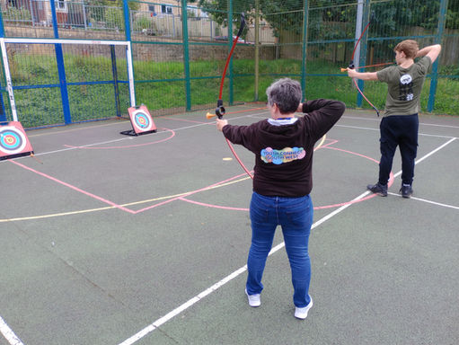 Two people practice archery, aiming at targets on a playing field.