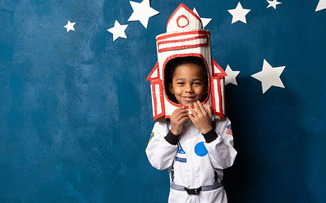 African-American boy in an astronaut costume stands against a background of a blue wall wi
