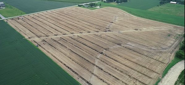 Aerial view of an agricultural field with neat rows and machinery working on drainage.