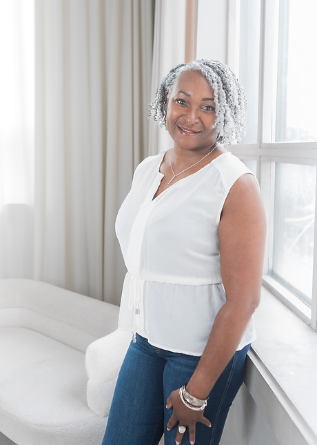 Sophia Murphy writer leaning against a window in a white shirt and jeans. Her face is turned toward the camera