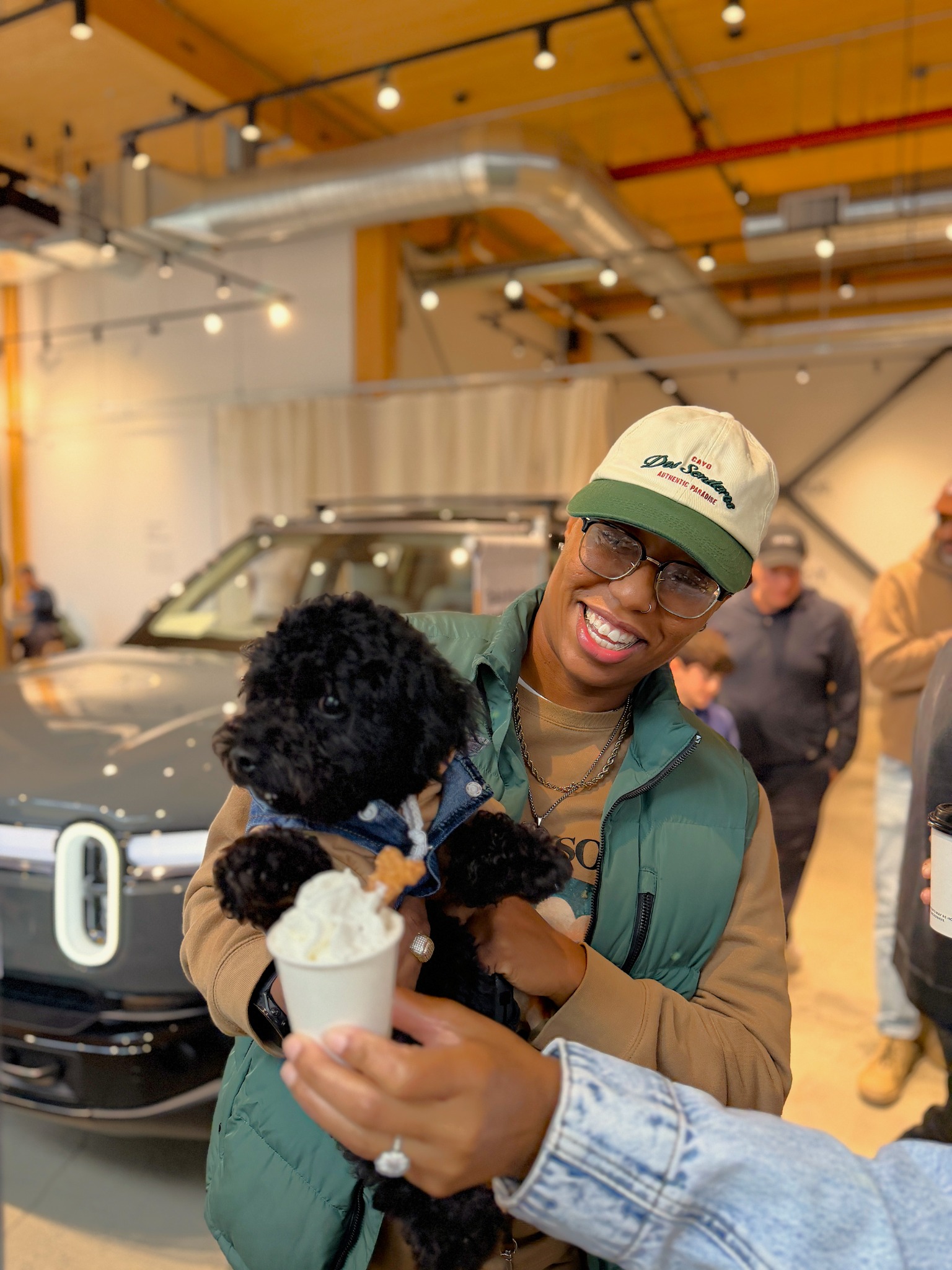 A smiling guest holding a black dog as a Barkaccino is offered at Rivian Williamsburg