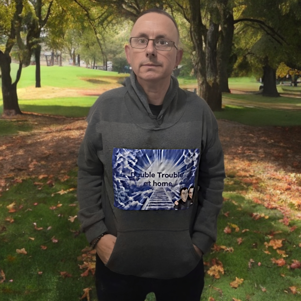 Middle-aged man in a hoodie with "Double Trouble" logo in park setting.
