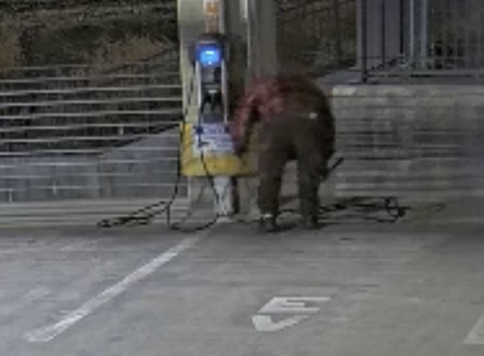 Homeless man cutting cables from EV charging station.