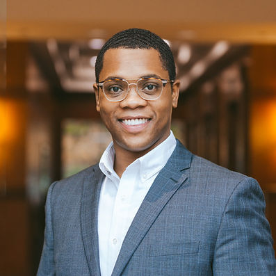 The founder DaJon smiling facing forward with glasses in a gray blazer and white collared shirt from the chest up. 