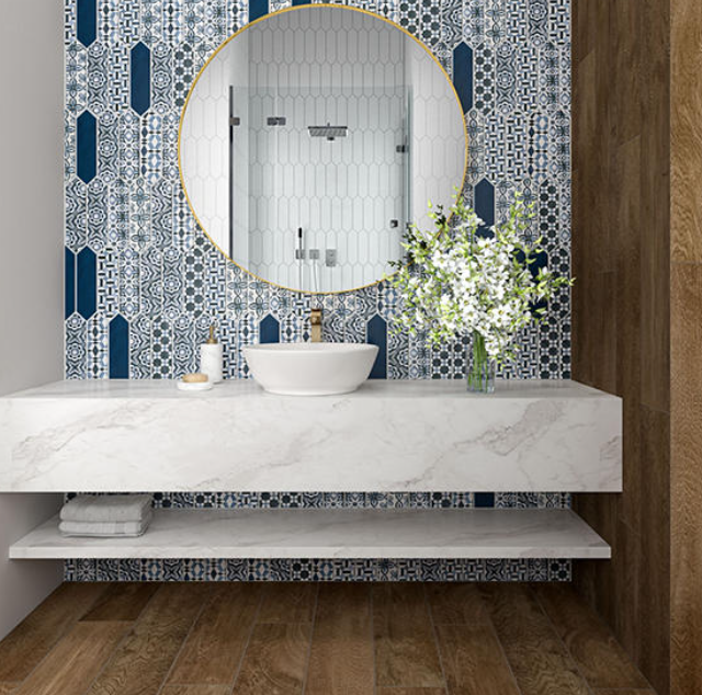 Vanity with white marble countertop, round gold-framed mirror, and blue patterned mosaic tile backsp