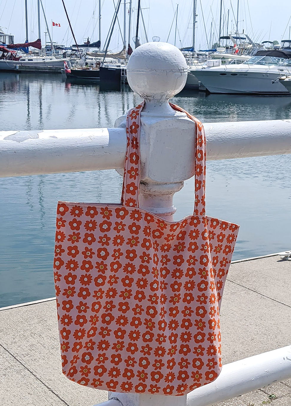 An orange bag hanging on a railing in front of water and boats.