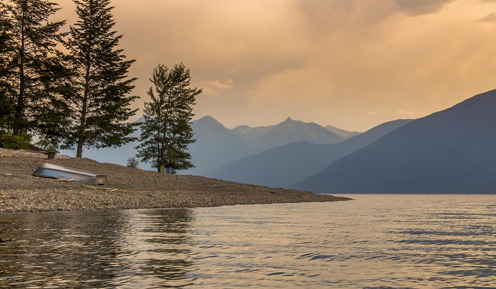 A photo of an overturned boat on the rocky shore of Kootenay Lake in the evening.