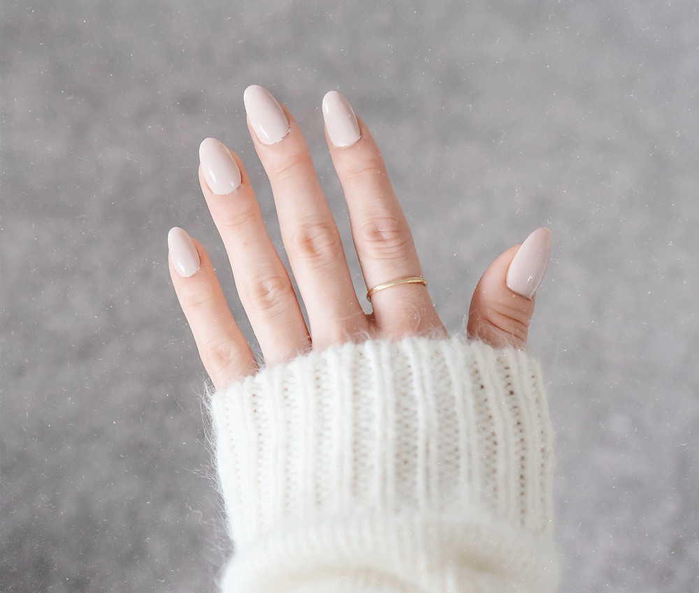 nailbliss press-on acrylic nails in almond against a grey carpet and morgan is wearing a white kit sweater