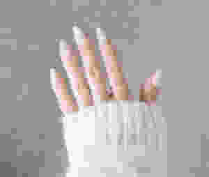 nailbliss press-on acrylic nails in almond against a grey carpet and morgan is wearing a white kit sweater