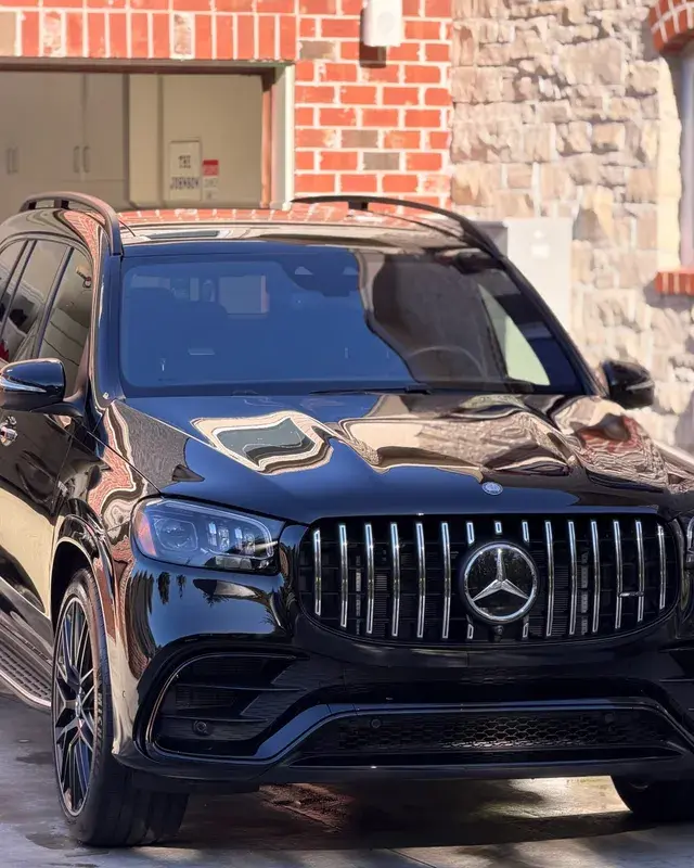 Black Mercedes GLS63 AMG SUV parked in front of a brick house, front view