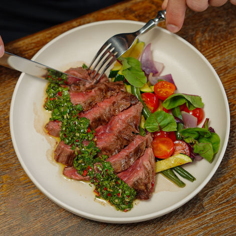 Steak, chimichurri sauce with a salad on a white plate fork and knife