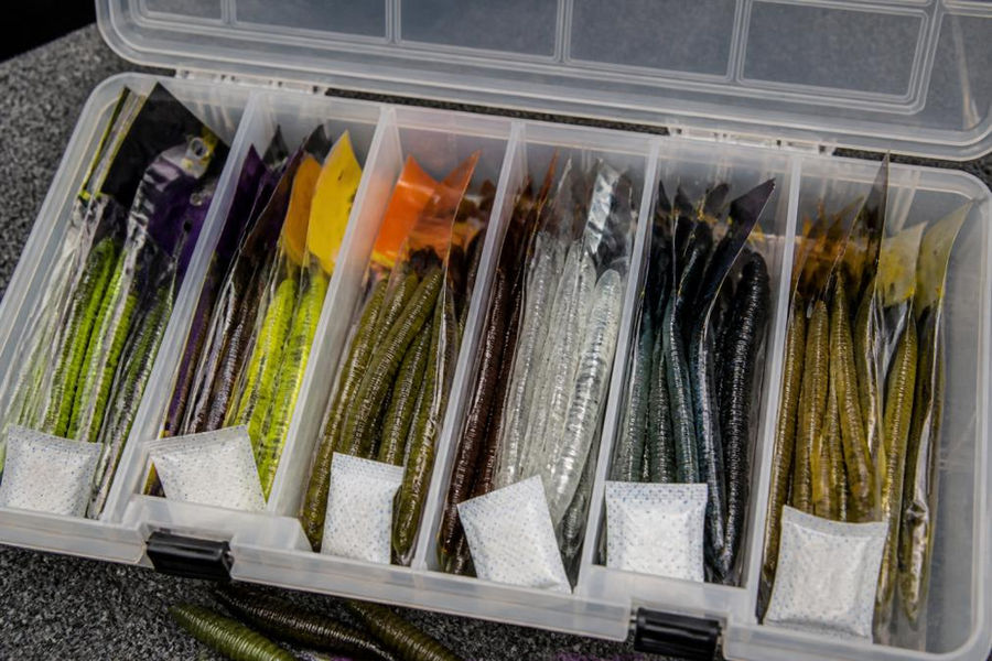 Close-up of a well-organized tackle box with soft plastic baits in original packaging, divided compartments, and silica gel packets visible