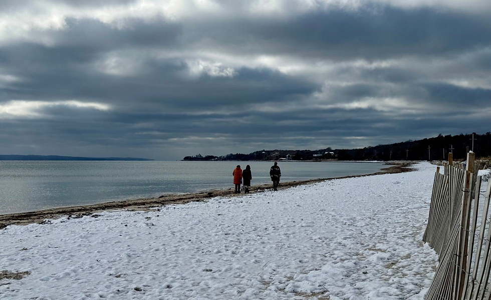 People walking together on a quiet Cape Cod beach in winter, with snow along the shoreline and calm ocean water.