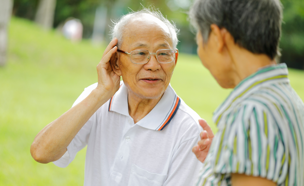 Older man outdoors, cupping his hand to his ear while trying to hear a woman speaking to him.
