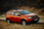 2 jante Dacia - un SUV Dacia Duster de culoare rosu portocaliu pe un drum de munte