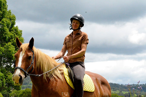Woman riding a chestnut brumby horse in a bitless bridle