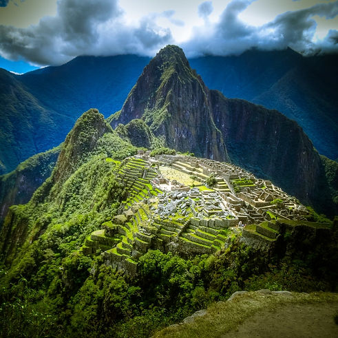 Majestic view of Machu Picchu, the ancient Incan citadel, perched high in the Andes Mountains of Peru, surrounded by lush green peaks under a dramatic cloudy sky.