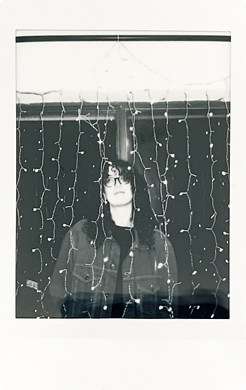 Black and white polaroid of a female standing amongst fairy lights
