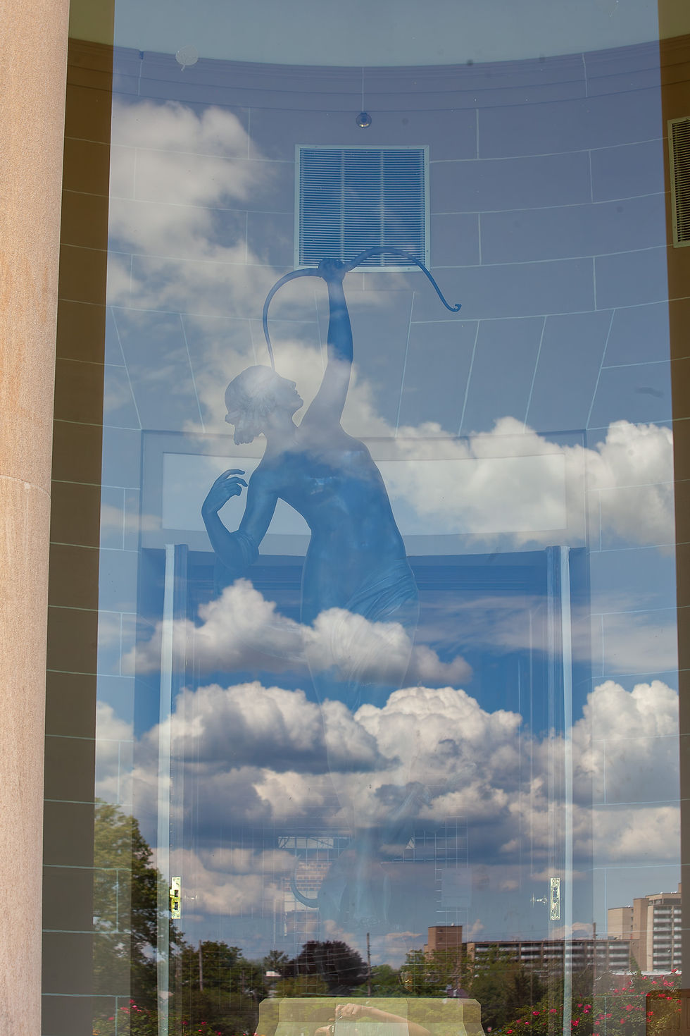 The sky and the "Boy with the Leaky Boot" statue are reflected in a window of the Arts and Entertainment Building in Hagerstown City Park.