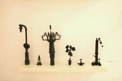 Three black sculptural objects resembling industrial taps or miniature architectural forms