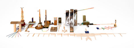 Horizontal installation of assorted wooden and metal objects – rods, columns, tool-like forms, colorful sticks.