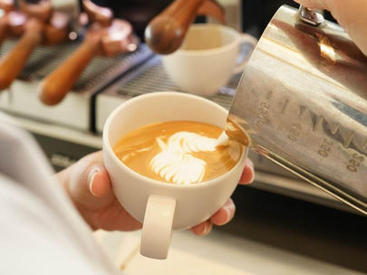 Participants pour microfoam into espresso to create the design of a heart and a flower on the surface of the coffee