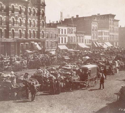 Historical photo of farm market sales on horse drawn carriages on downtown street.