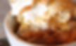 Closeup of a warm peach cobbler dessert within a white bowl topped with ice cream and cinnamon.