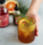 A botanical negroni in a pretty orange glass with raised bumps on the outside. There is an orange slice and fennel frond for a garnish.