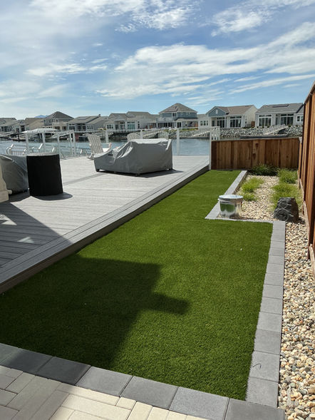Luxury waterfront backyard with artificial grass, belgard midnight paver borders, and salt and pepper gravel landscaping overlooking the water in Bethel Island, CA.