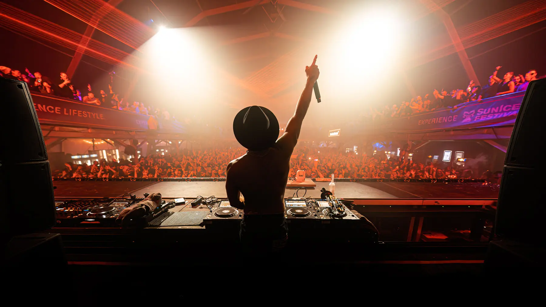 Timmy Trumpet hebt seine Hand  in der er sein Mikrofon hält , die Scheinwerfer Beleuchten ihn