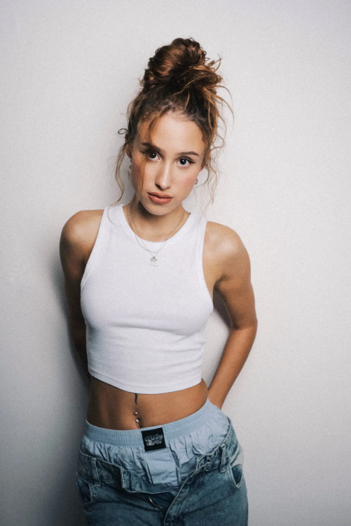 Frau mit Braunen Haaren steht an der Wand in einem Fotostudio und Schaut Richtung Kamera