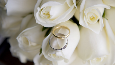 A photographt of white roses with a pair of wedding bands laid over the top