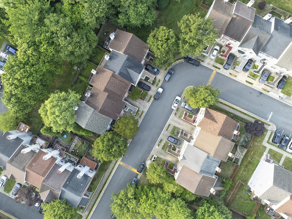 Aerial view of a leafy suburban neighborhood with houses, parked cars, and curving streets under dense green trees.