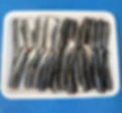 Fresh sardine fillets with silver skin and pink flesh, selectively arranged on a white tray.