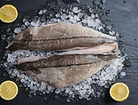 Four fresh haddock fillets on a black slate board garnished with coarse sea salt and dill.