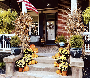 Front porch of a brick house, decorated with yellow mums, pumpkins and corn shocks