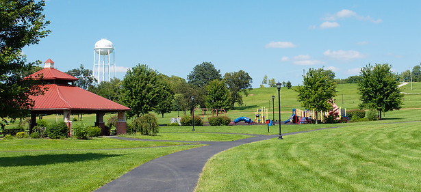 Summer day at Flat Run Veterans Park, showing the picnic shelter, walking trail, and playground with a Cynthiana water tower in the distance