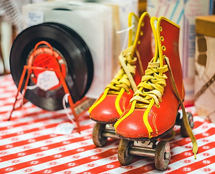 Pair of vintage roller skates set on a table with a red checked tablecloth and a stack of 45 records
