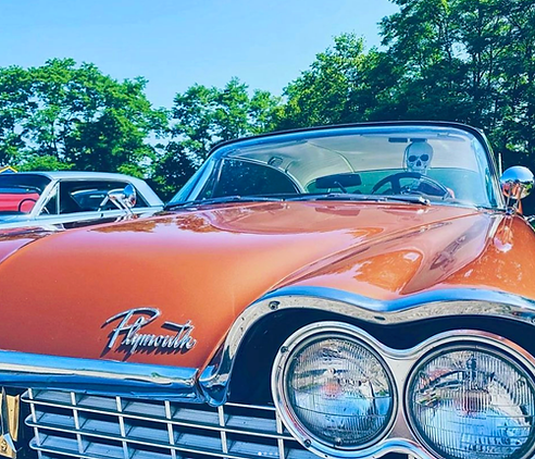 Front view of a classic Plymouth car with a skeleton seated in the driver's seat