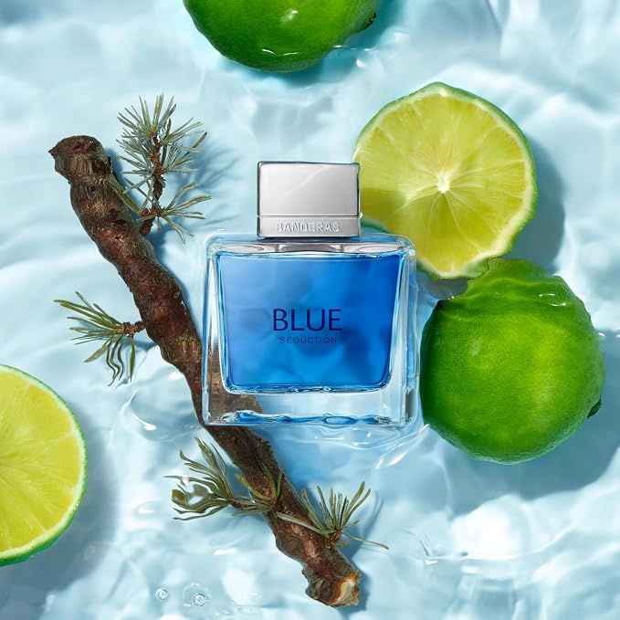 Frasco de perfume azul BLUE Seduction da Banderas cercado por limas e galho sobre água azul, em clima fresco.