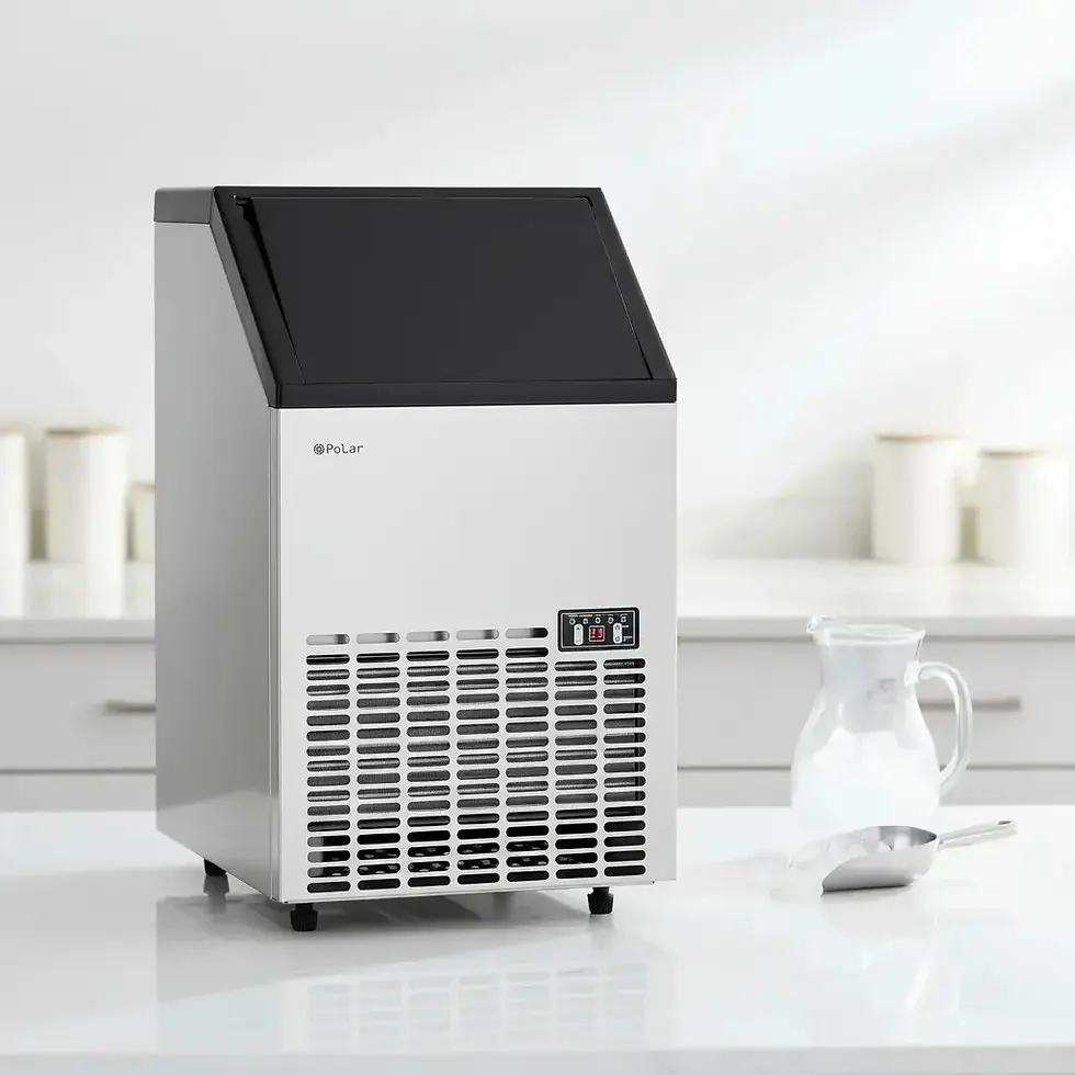 Máquina de gelo prateada da marca "Polar" em balcão branco. Ao lado, uma jarra de vidro e uma concha metálica. Ambiente de cozinha claro.