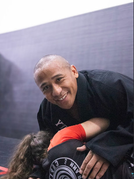 Smiling man in black gi holds down a person on mat