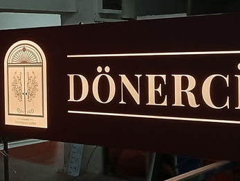 Koyu ahşap dokulu alüminyum kompozit zemin üzerine lazer derz oyma ve arkadan sıcak sarı LED aydınlatmalı Çarşıkapı Dönercisi ışıklı tabela.