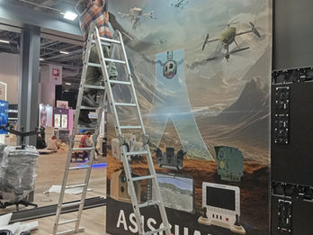 ASISGUARD firması fuar standı için özel hazırlanan, insansız hava araçları ve savunma sistemleri görsellerini içeren yüksek çözünürlüklü stand içi duvar panosu.