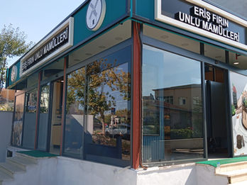 Eriş Fırın köşe mağaza dış cephesine yapılan koyu yeşil kompozit giydirme, dairesel ışıklı logolar ve vitrin camı üzeri yüksek çözünürlüklü ürün görselleri folyo kaplaması.