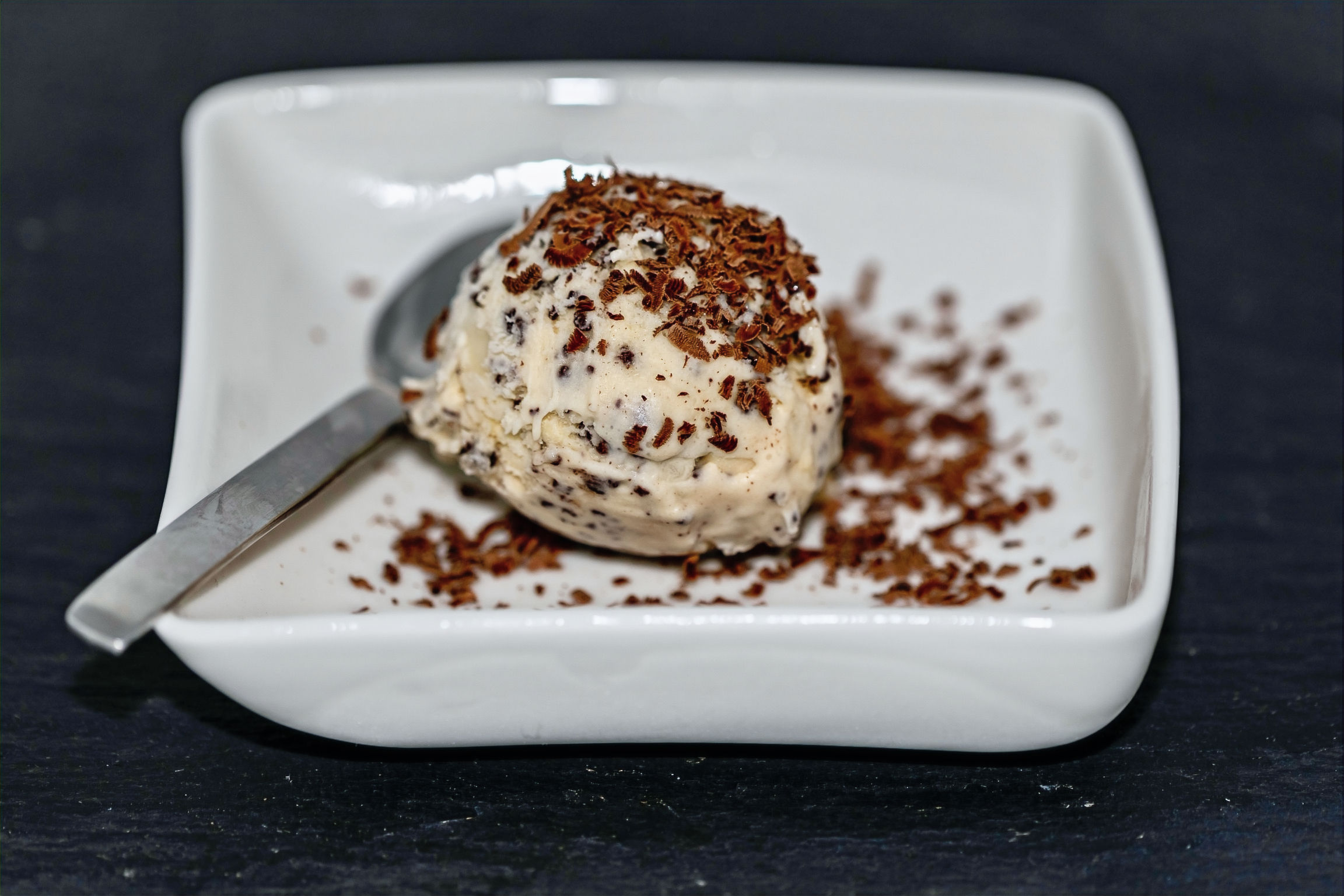 Kugel Stracciatellaeis in einer weißen Schale, bestreut mit Stracciatellastückchen.